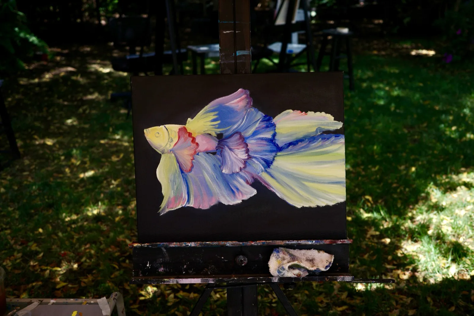 Oil painting of a pale betta fish with flowing lavender, blue, and yellow fins on a dark canvas.
