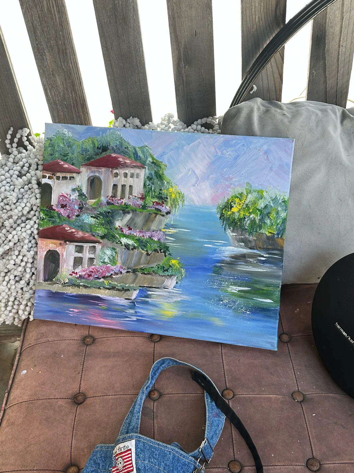 Oil painting of red-roofed houses, flowers, and green islands beside blue water.